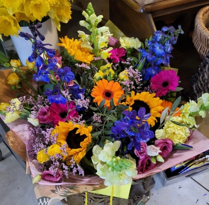 Selection of blue delphiniums and bright sunflowers with complementary flowers and foliages to create amazing summer display in the interior.